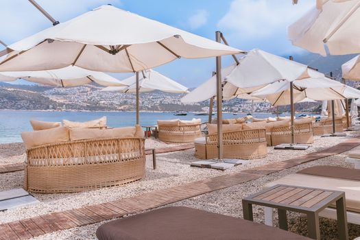 Relaxing seaside lounge with wicker chairs and sunshades on a pebble beach overlooking the sea.