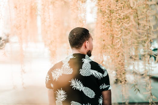 一名穿着夏威夷衬衫的男子站在垂挂的树叶间，营造出梦幻而模糊的户外场景