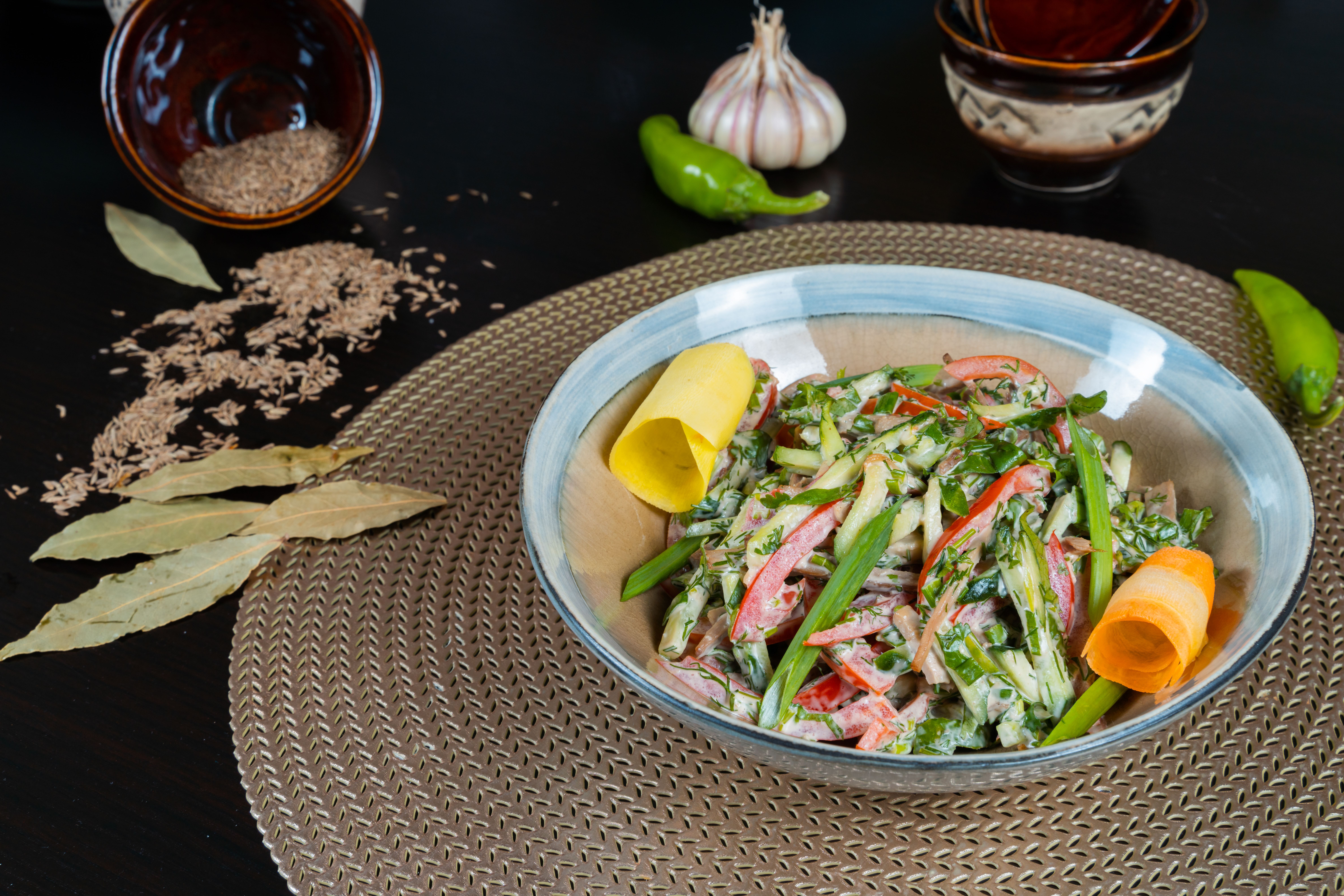 A colorful veggie salad with herbs on a woven mat, featuring peppers and spices.