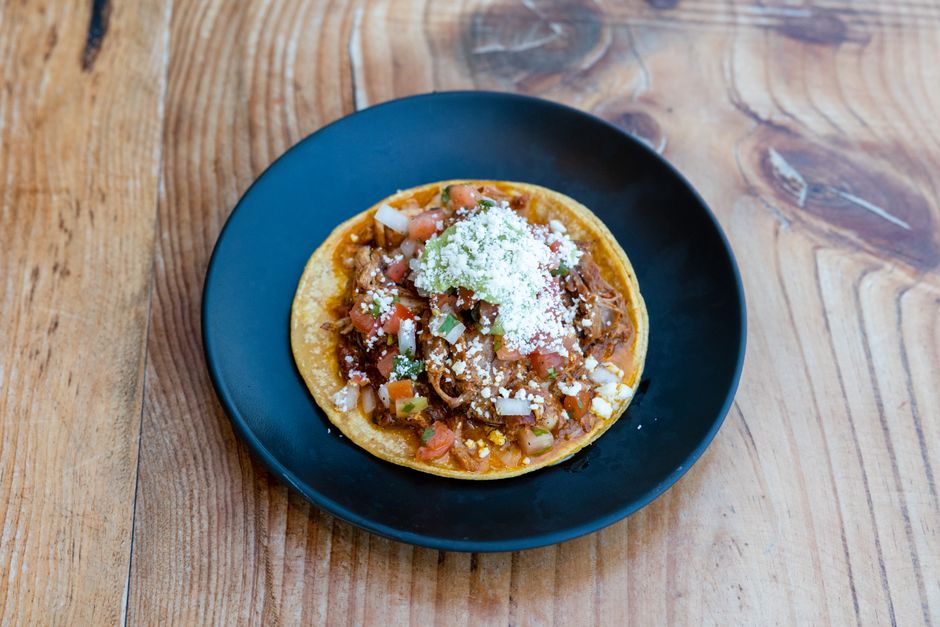 Shredded chicken tinga in smoky red chipotle sauce piled onto crisp tostadas with crema, avocado, and pickled onion.