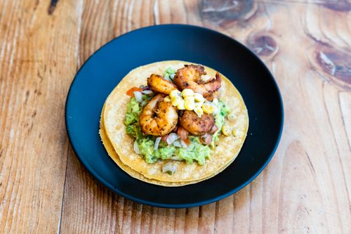 Free Mouthwatering shrimp tacos with guacamole served on a rustic wooden table, perfect for a vibrant meal. Stock Photo