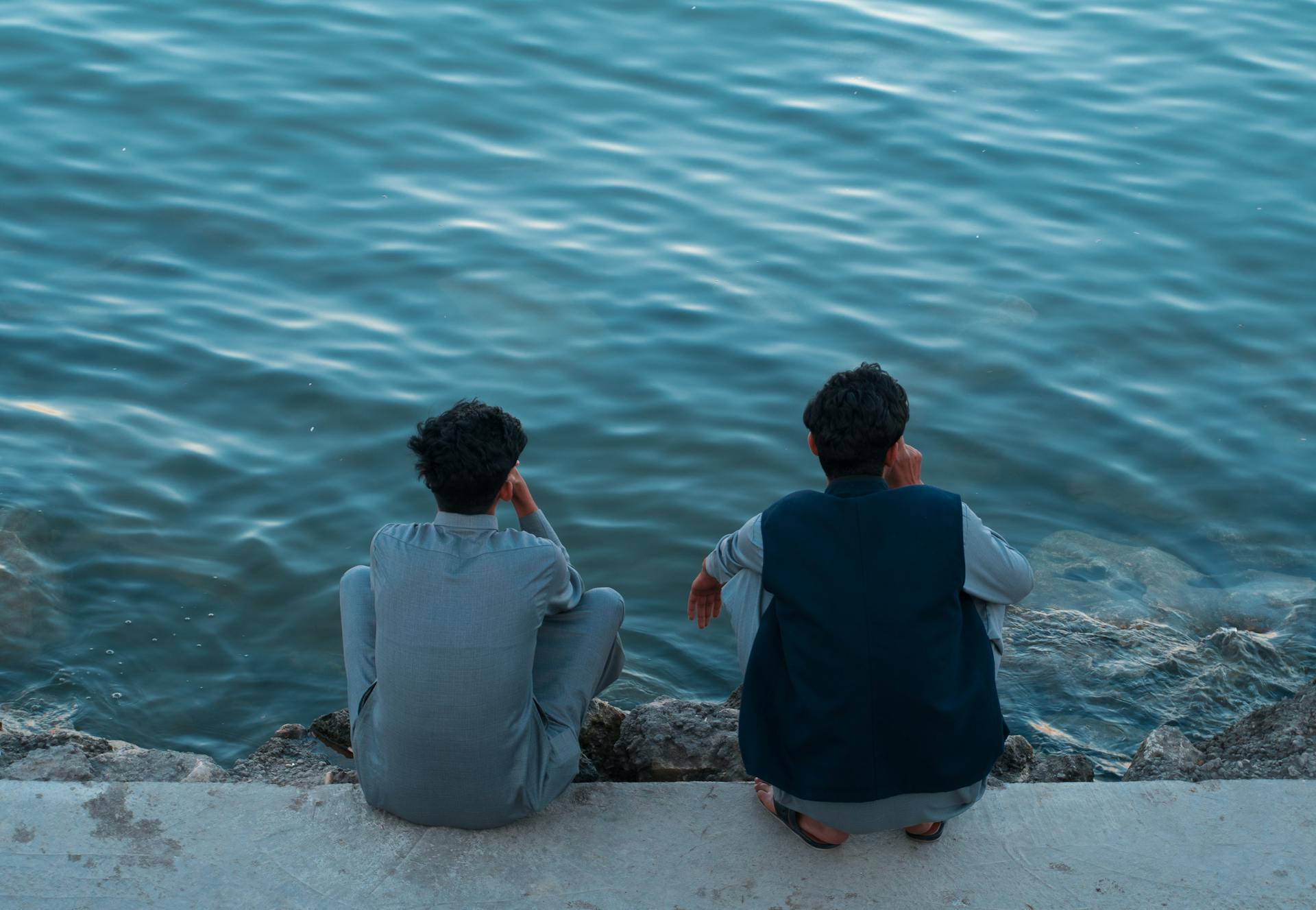 Two men in traditional clothing sit by the water in Basrah, Iraq, enjoying a serene moment.