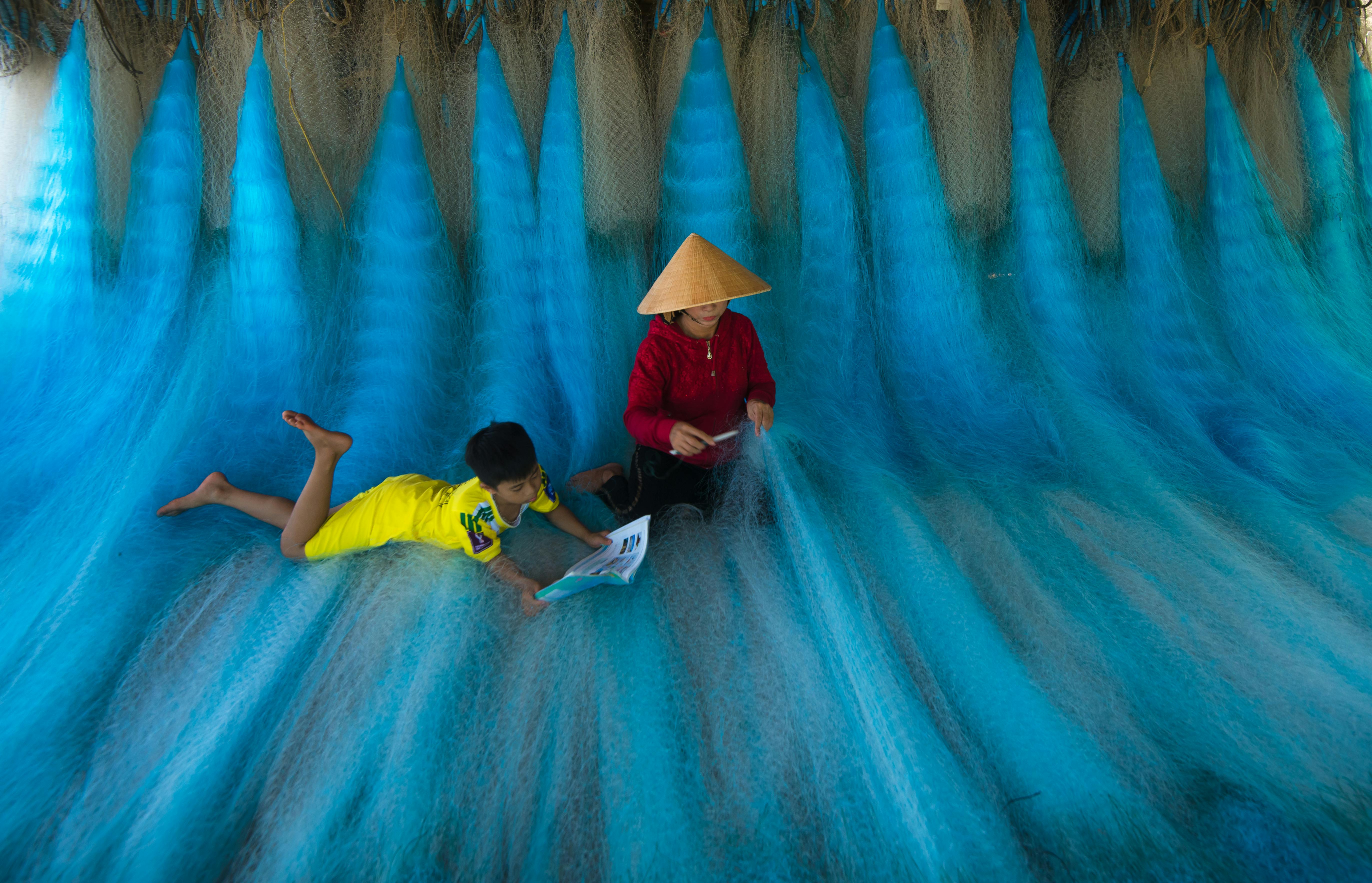 A child and woman working with vibrant blue fishing nets in Hội An, Vietnam.