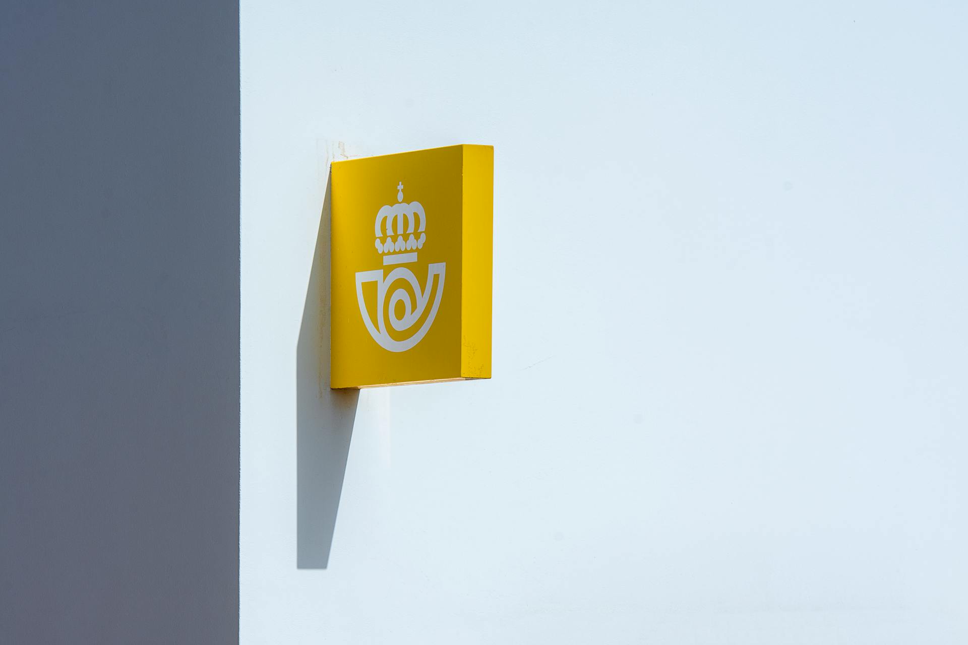 Yellow postal sign on a white wall with clear sky. Captured in Lanzarote, Spain.