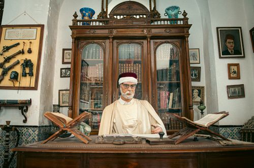 Free Vintage-style interior of a Tunisian library with a traditionally dressed figure and antique decor. Stock Photo
