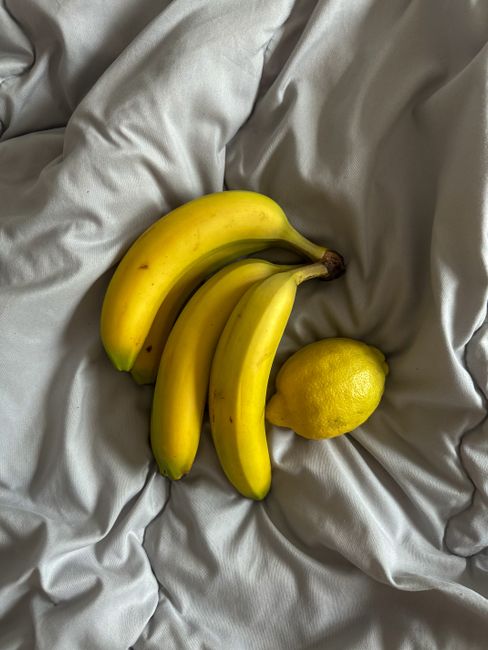 A trio of bananas and a lemon on soft gray fabric, highlighting freshness.