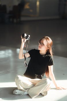 Casual portrait of a young woman sitting on the floor indoors, holding a camera.