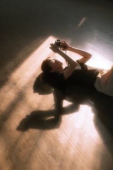 Silhouetted person lying on the floor holding a device, backlit by sunlight creating a dramatic shadow.