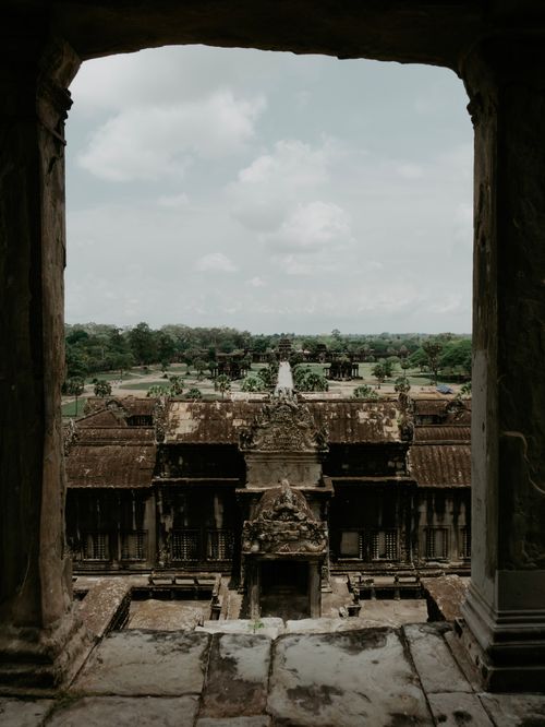 Free Experience the majestic view of Angkor Wat through a historic window in Siem Reap, Cambodia. Stock Photo
