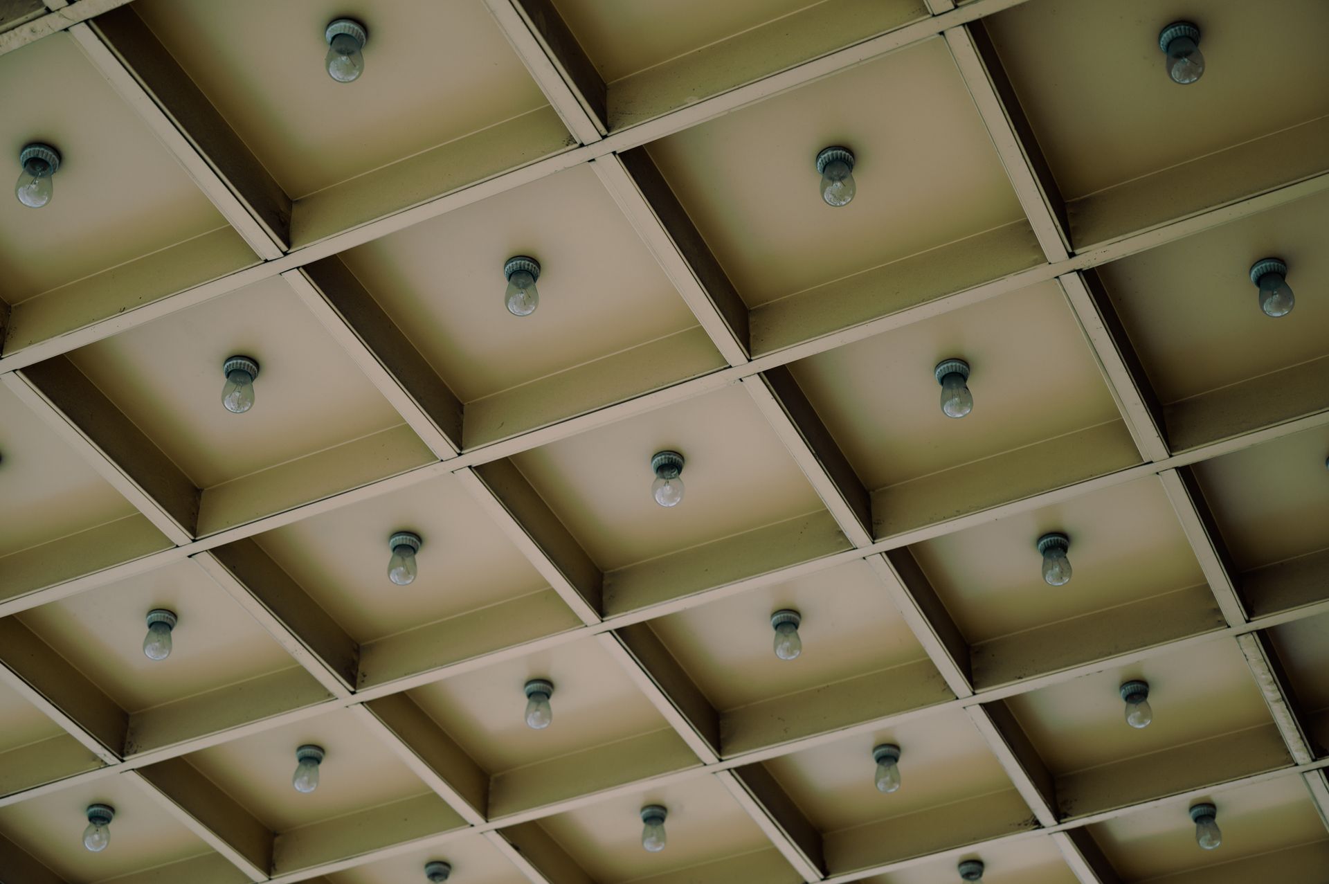 A modern geometric ceiling design featuring a grid pattern with light bulbs for architectural aesthetics.
