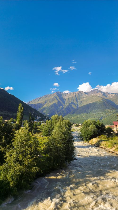 Free A beautiful mountain river flowing through a lush green valley under a clear blue sky. Stock Photo