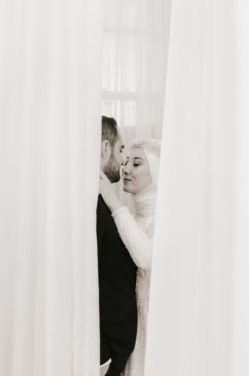 Free A bride and groom share a tender moment behind white curtains, symbolizing love and intimacy. Stock Photo