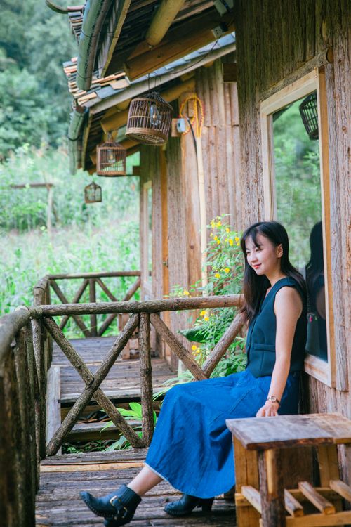 Free Young woman sitting on a rustic wooden porch, enjoying a peaceful outdoor setting. Stock Photo