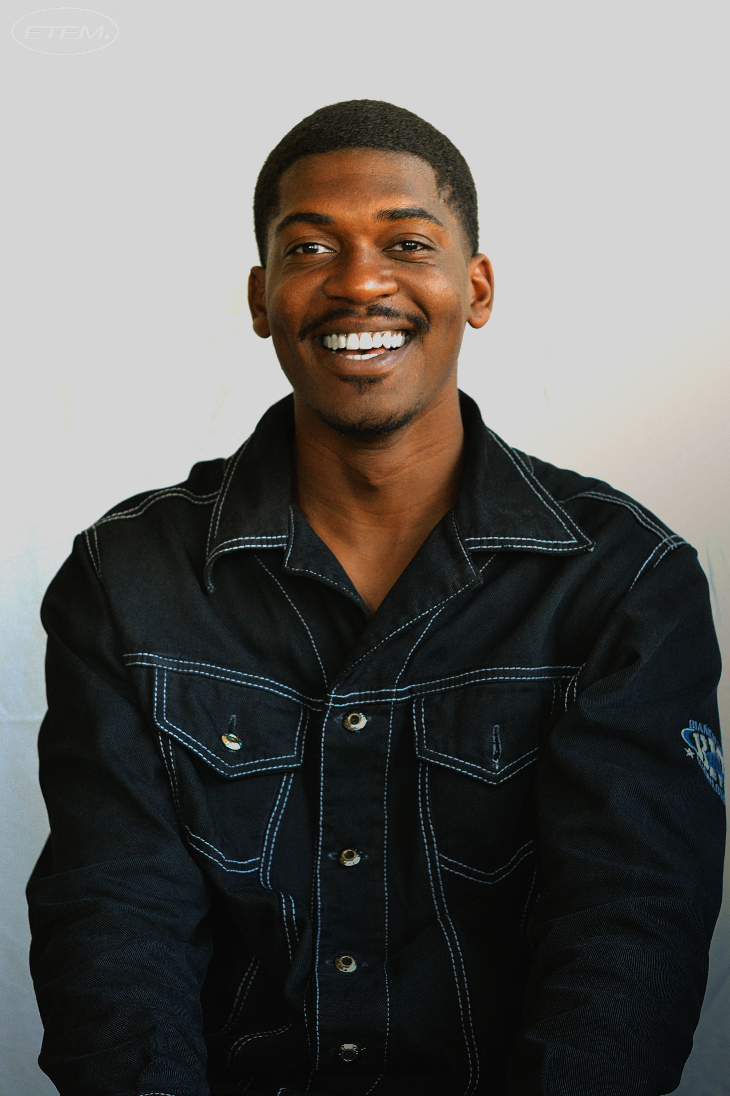 Portrait of a smiling man wearing a denim jacket against a neutral background.