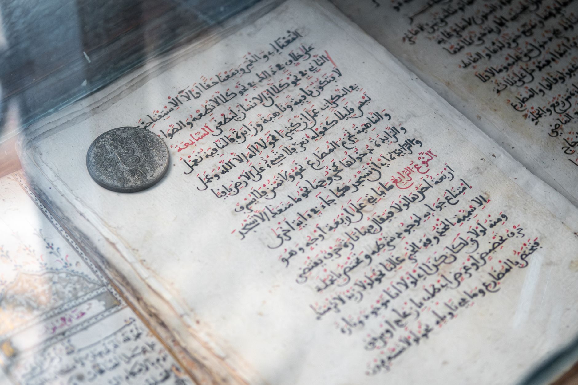Detailed view of an ancient Arabic manuscript and old coin on display, showcasing Islamic calligraphy.
