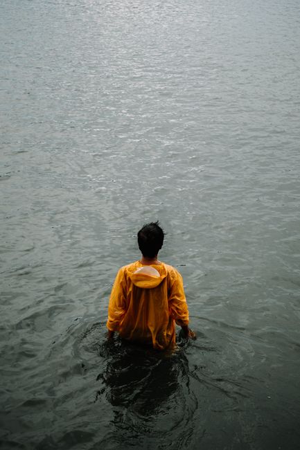 An individual in a yellow jacket stands alone in water, conveying solitude.