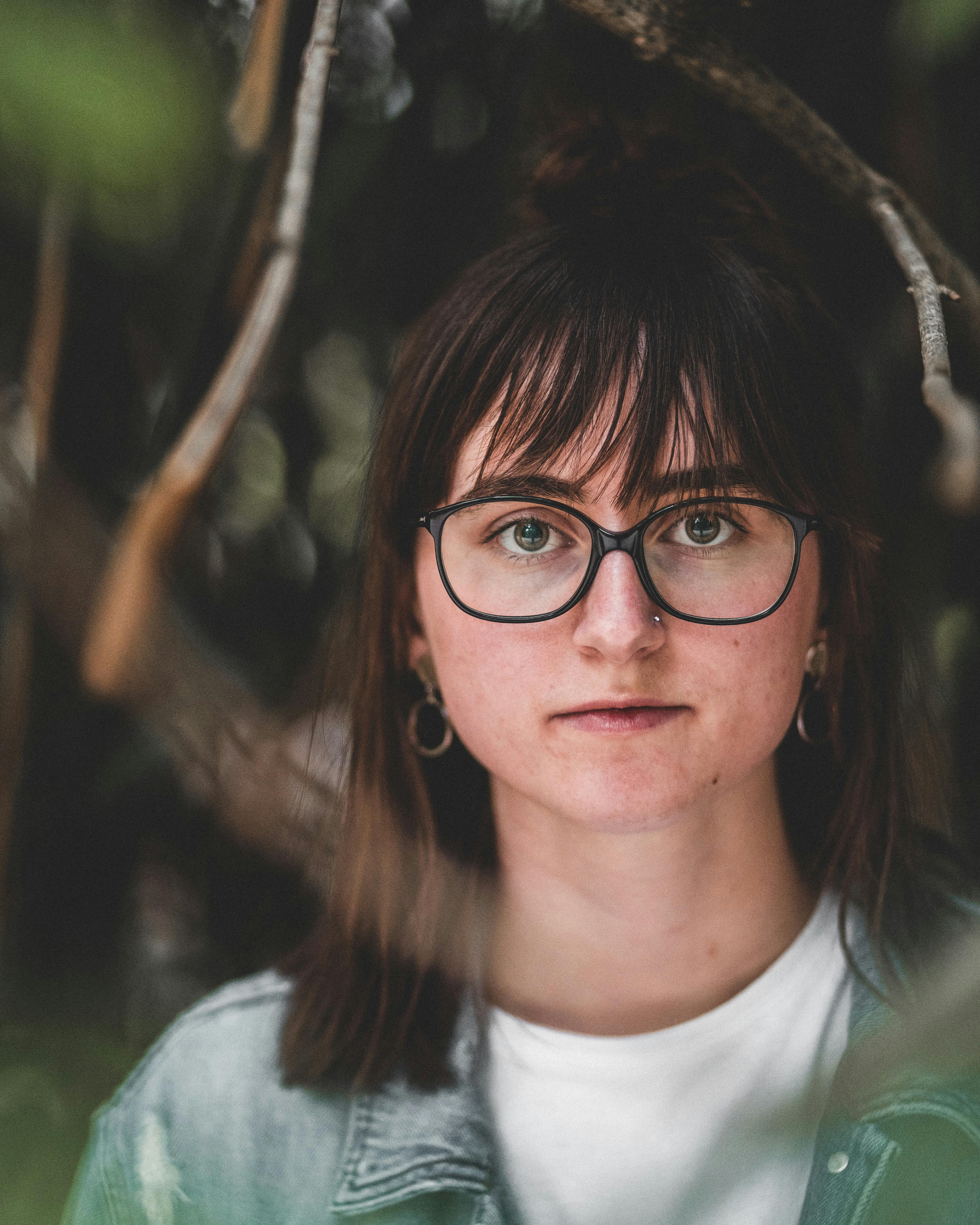 户外场景中，一位表情严肃、戴着眼镜、鼻子上有穿孔的妇女特写画像