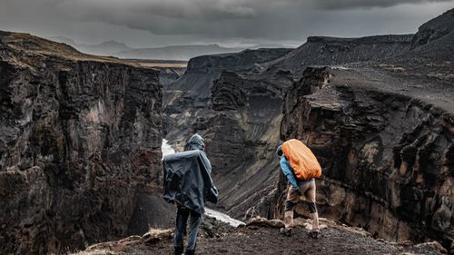 Free Two hikers explore a dramatic canyon landscape under cloudy skies, showcasing the rugged terrain. Stock Photo