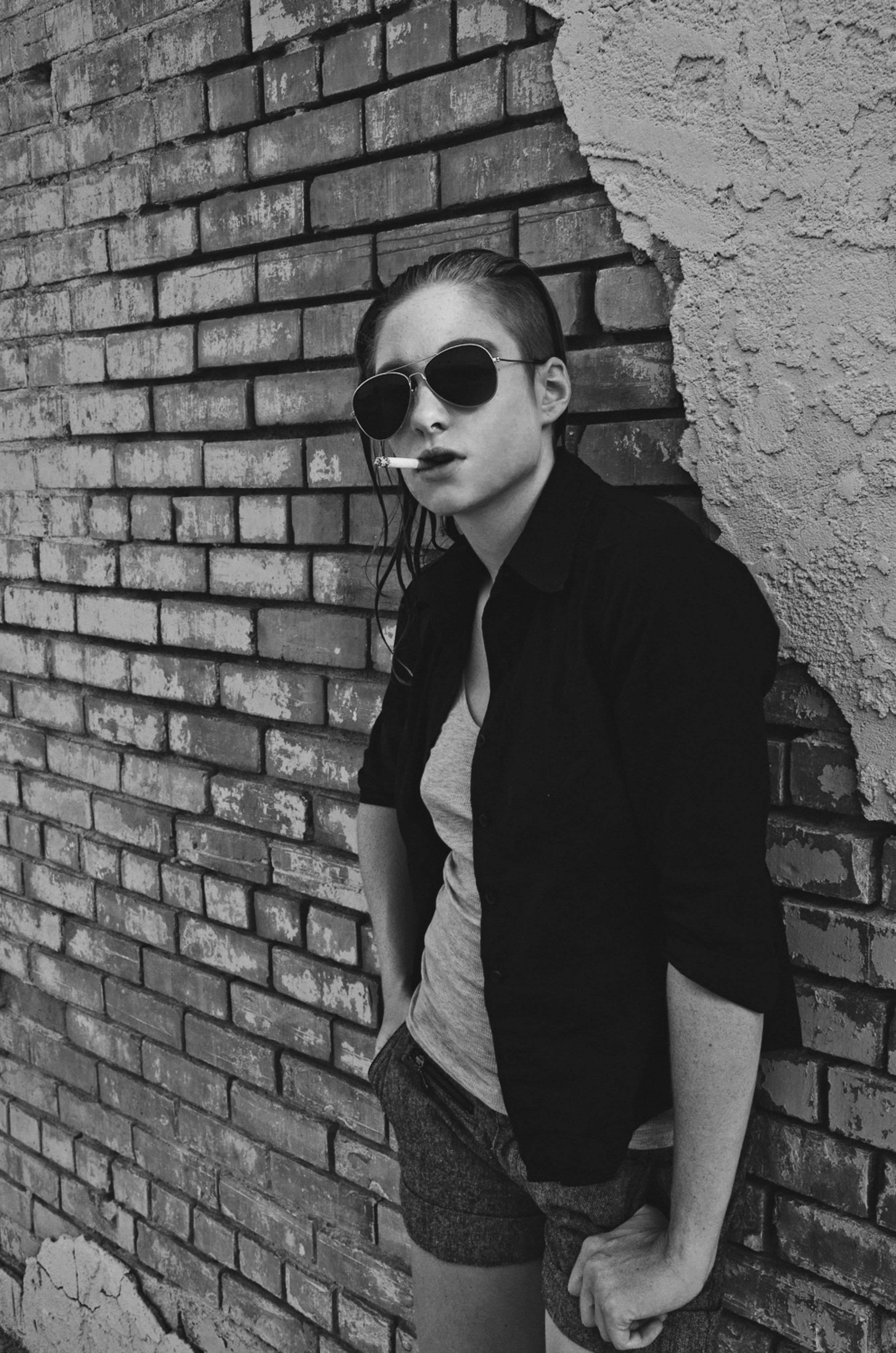 A woman in sunglasses leaning against a brick wall · Free Stock Photo
