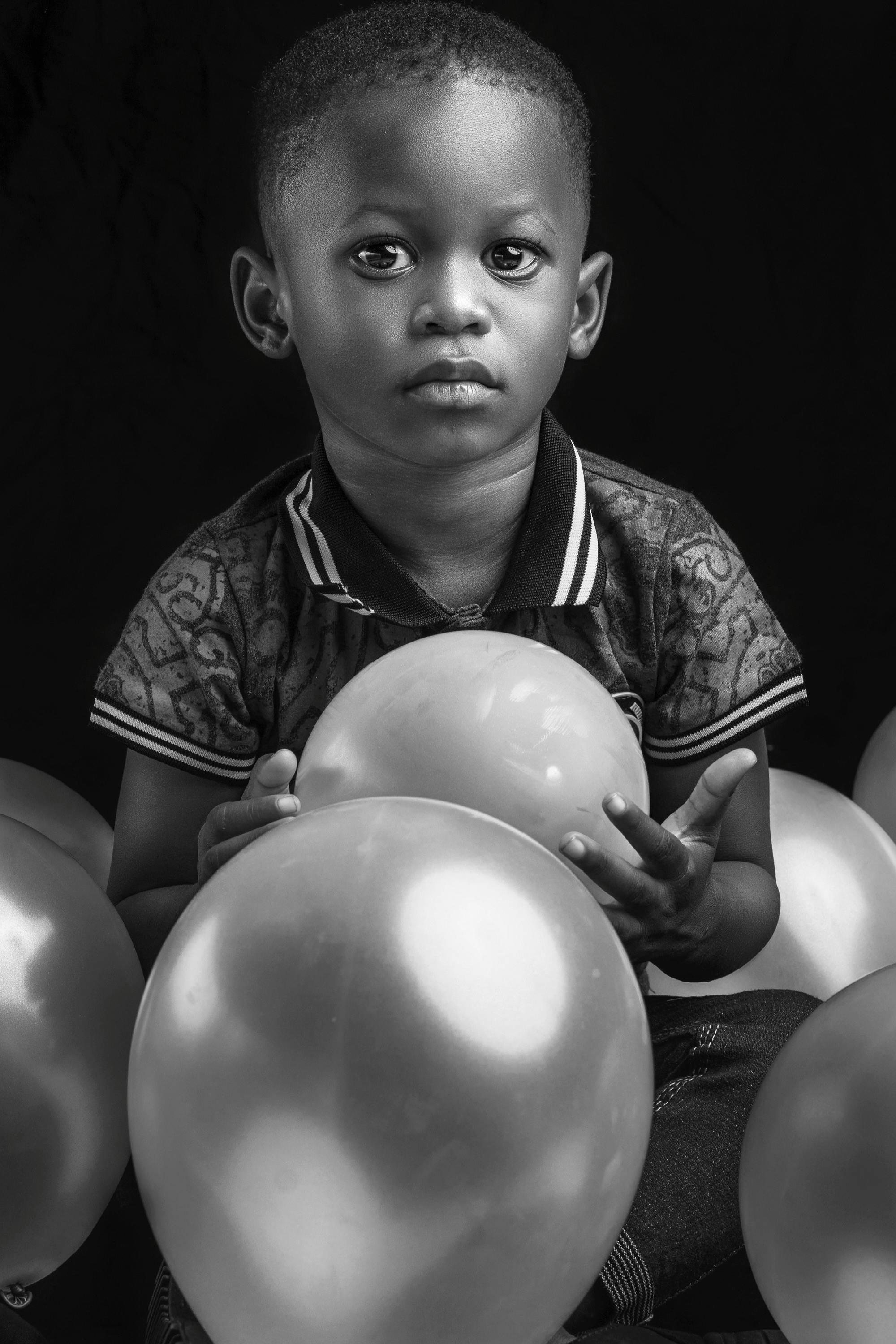 black and white photo of a young boy holding balloons