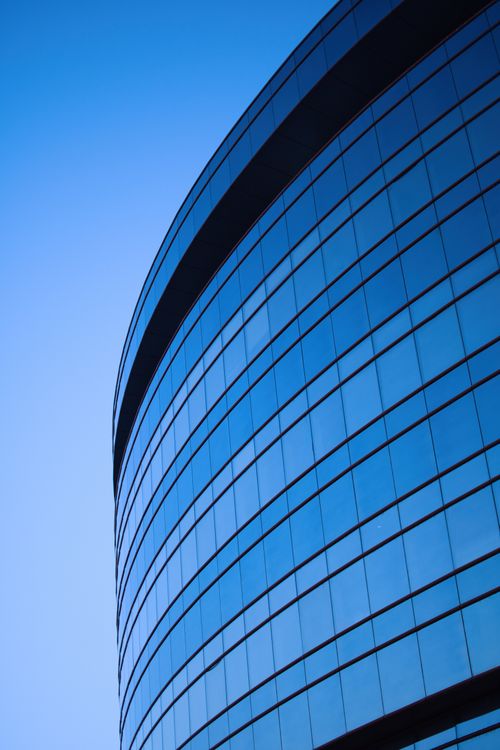 Free A contemporary skyscraper with a sleek curved glass facade reflecting the blue sky. Stock Photo