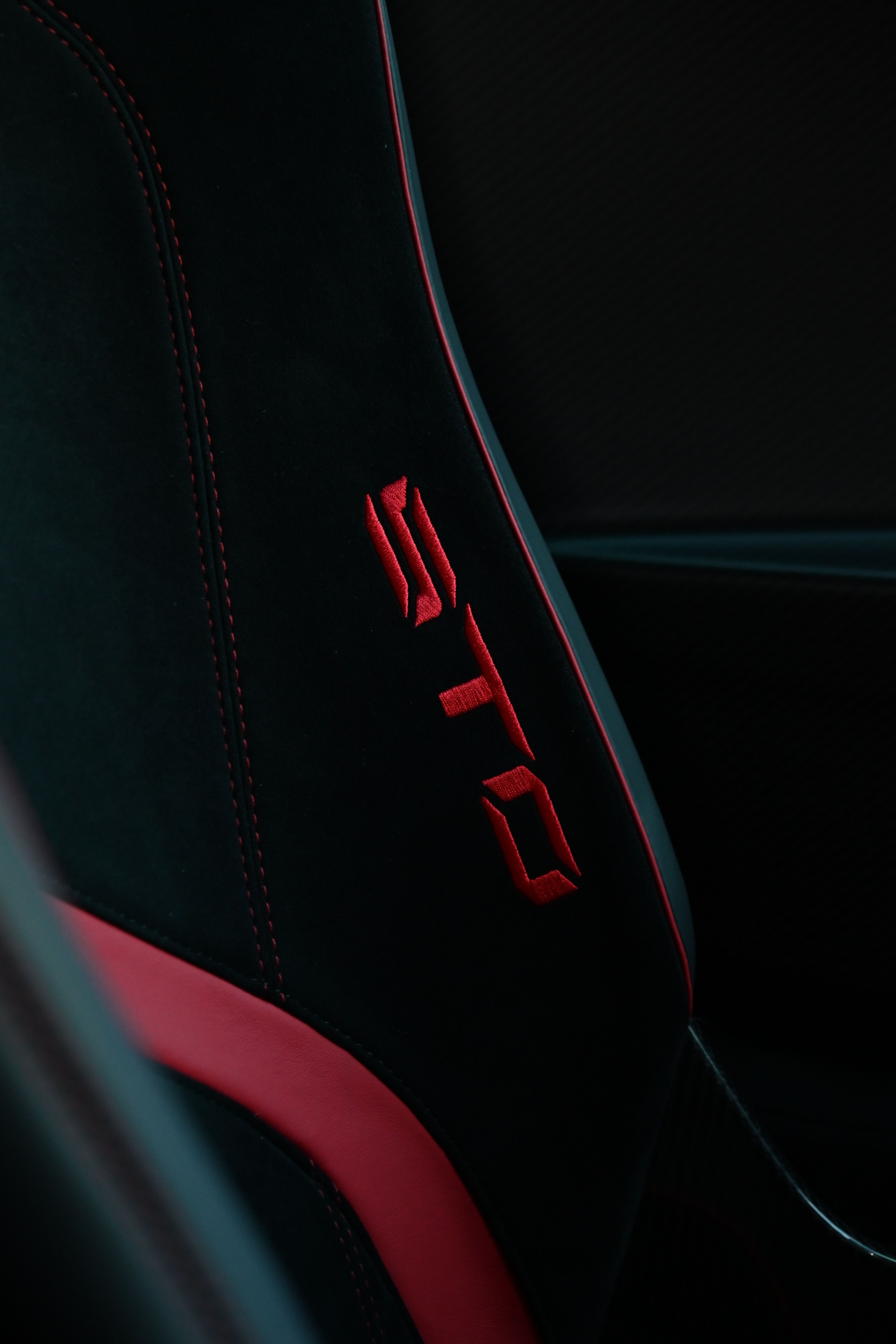 Detailed view of a black car seat with red stitching and a vibrant logo.