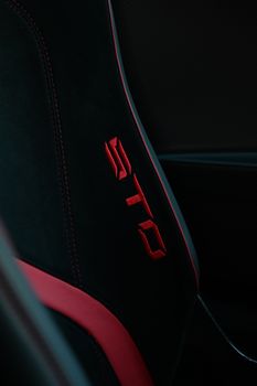 Detailed view of a black car seat with red stitching and a vibrant logo.