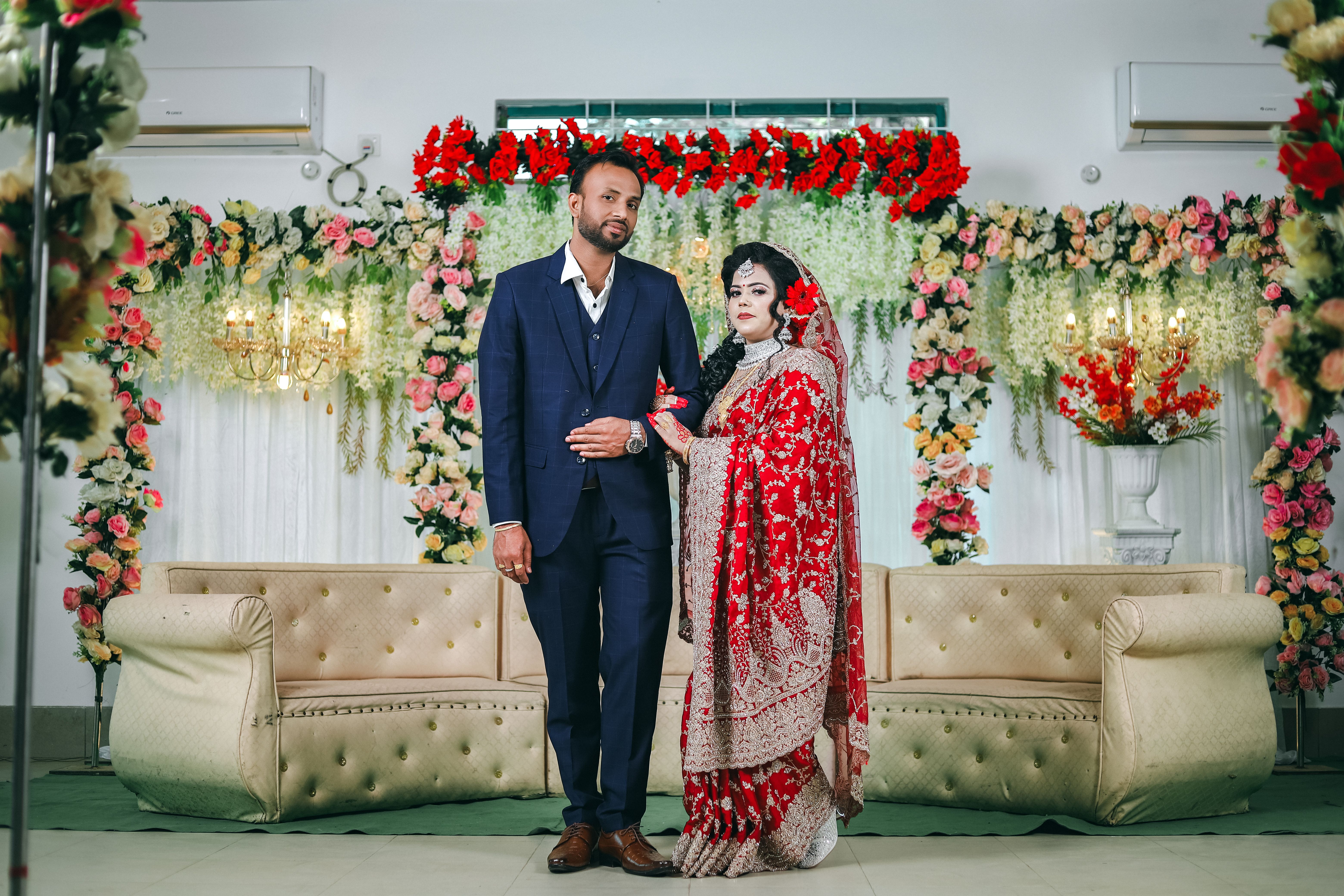 A bride and groom pose indoors with vibrant floral decorations at their wedding ceremony.