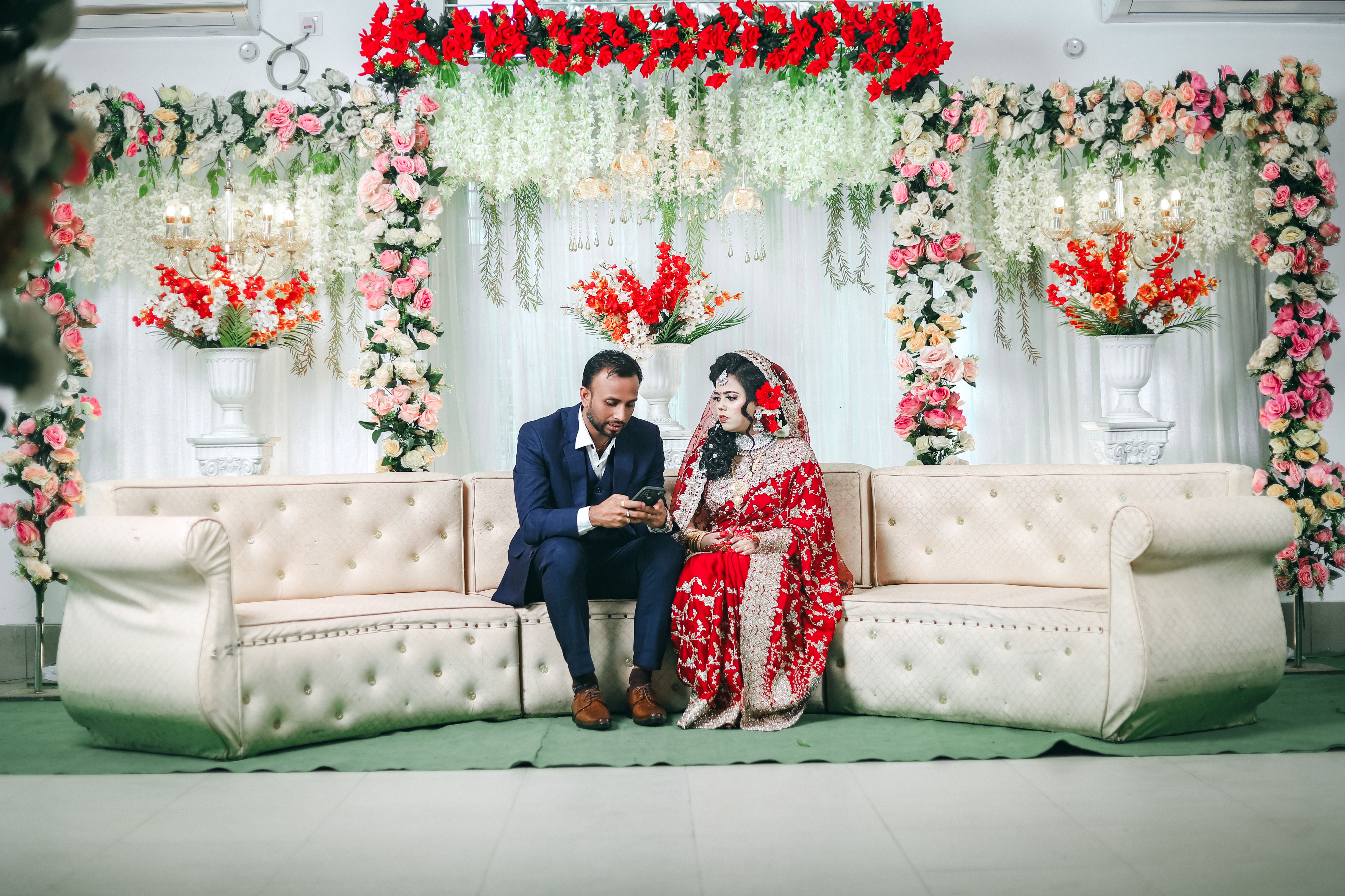 A beautiful Indian couple in traditional attire sitting in a floral decorated room, capturing a tender moment.