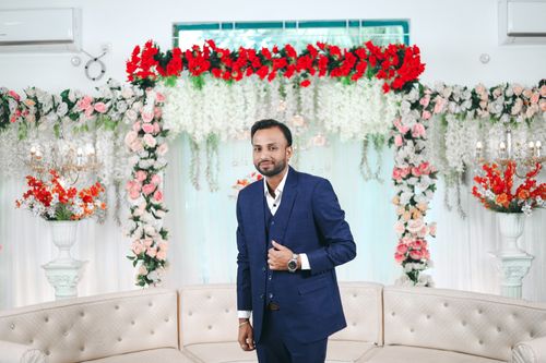 Free A portrait of a groom in formal attire, surrounded by vibrant floral decorations at an indoor wedding. Stock Photo