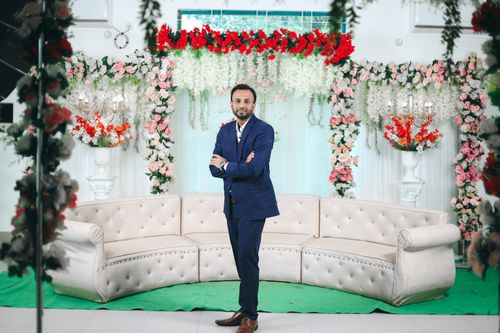 Free A man poses in a stylish suit amidst elegant wedding decorations featuring vibrant floral arrangements. Stock Photo