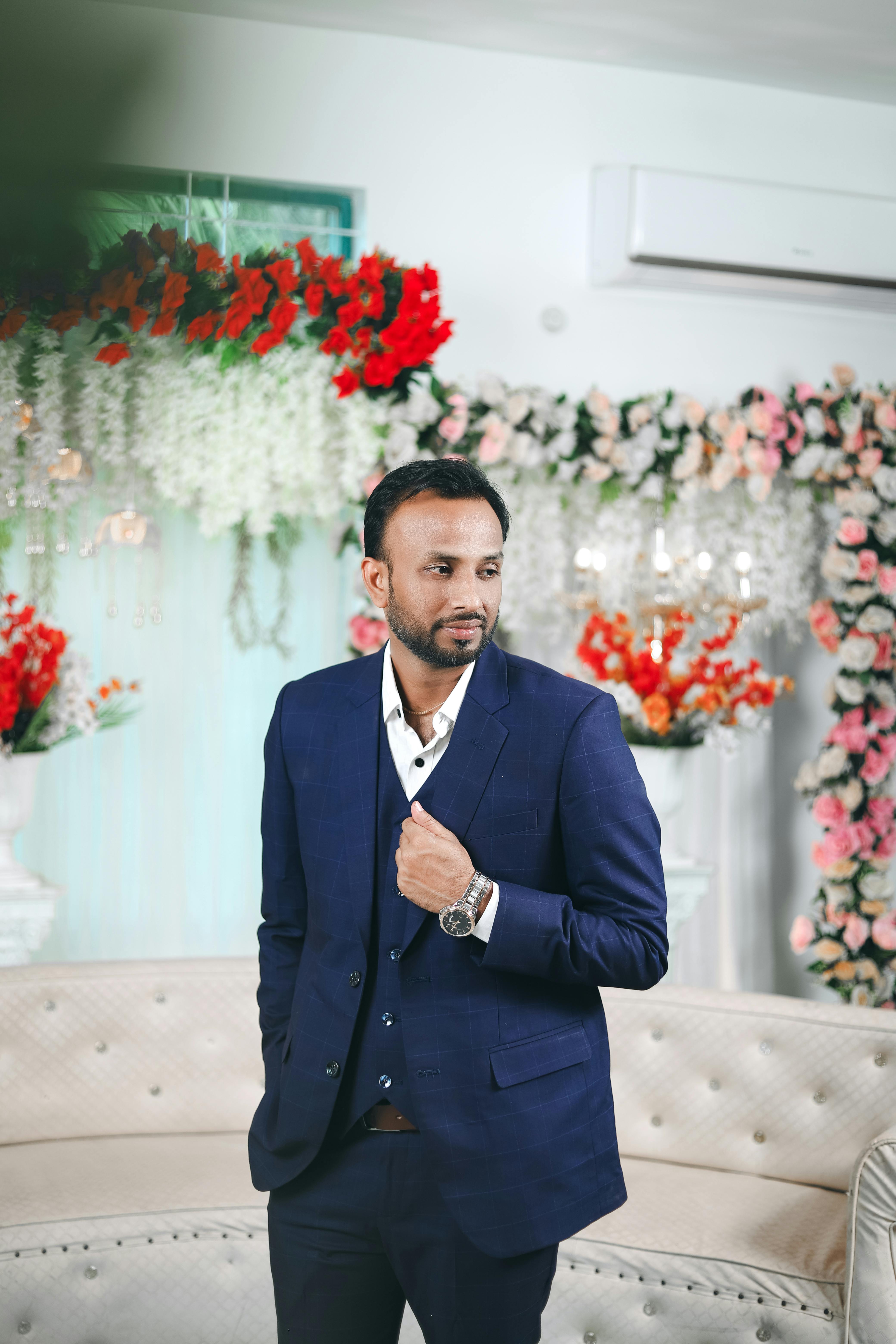 Handsome groom in a tailored suit, surrounded by floral decorations at an indoor wedding.