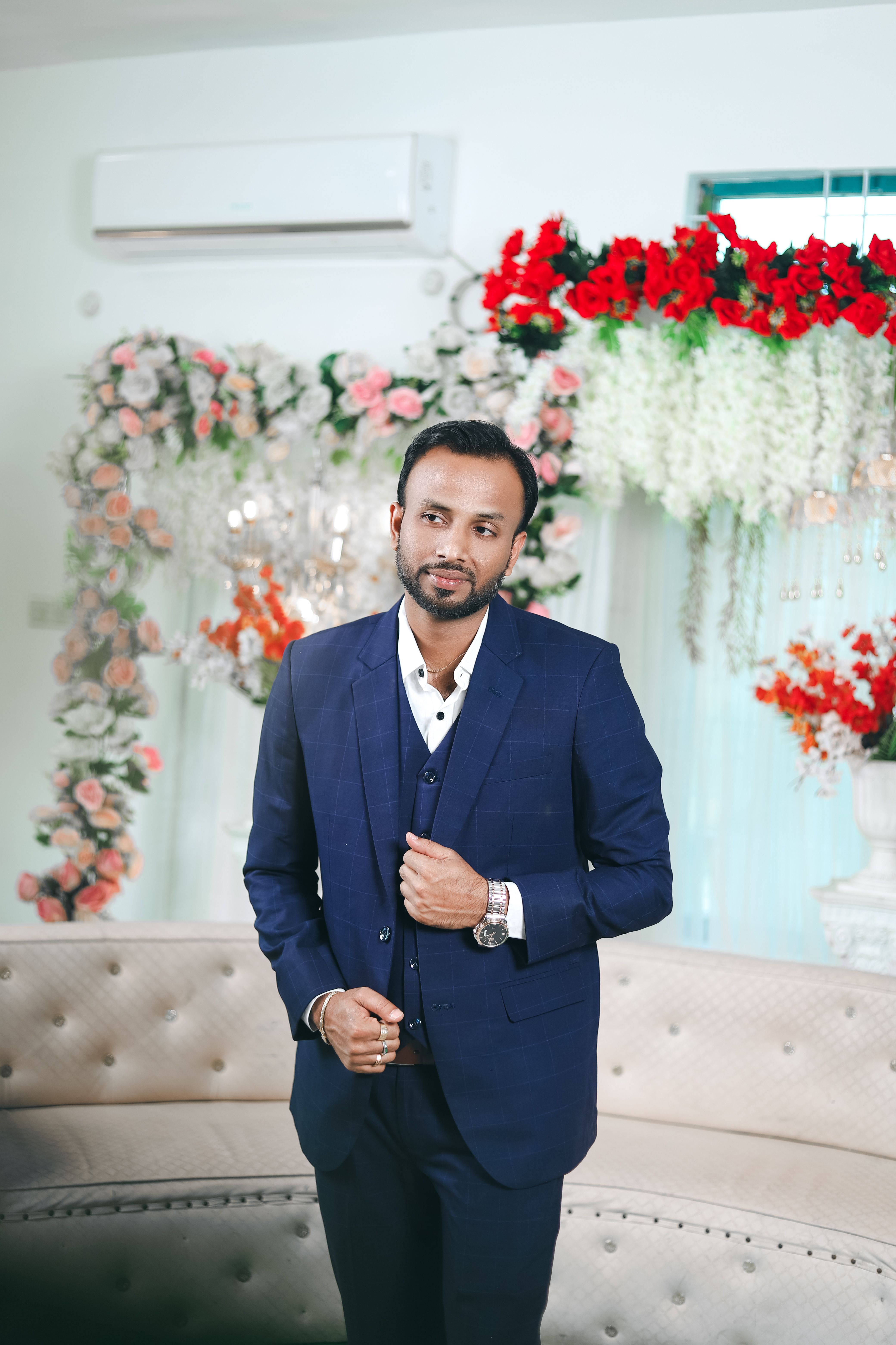 Stylishly dressed groom in a blue suit poses at an indoor Indian wedding ceremony.