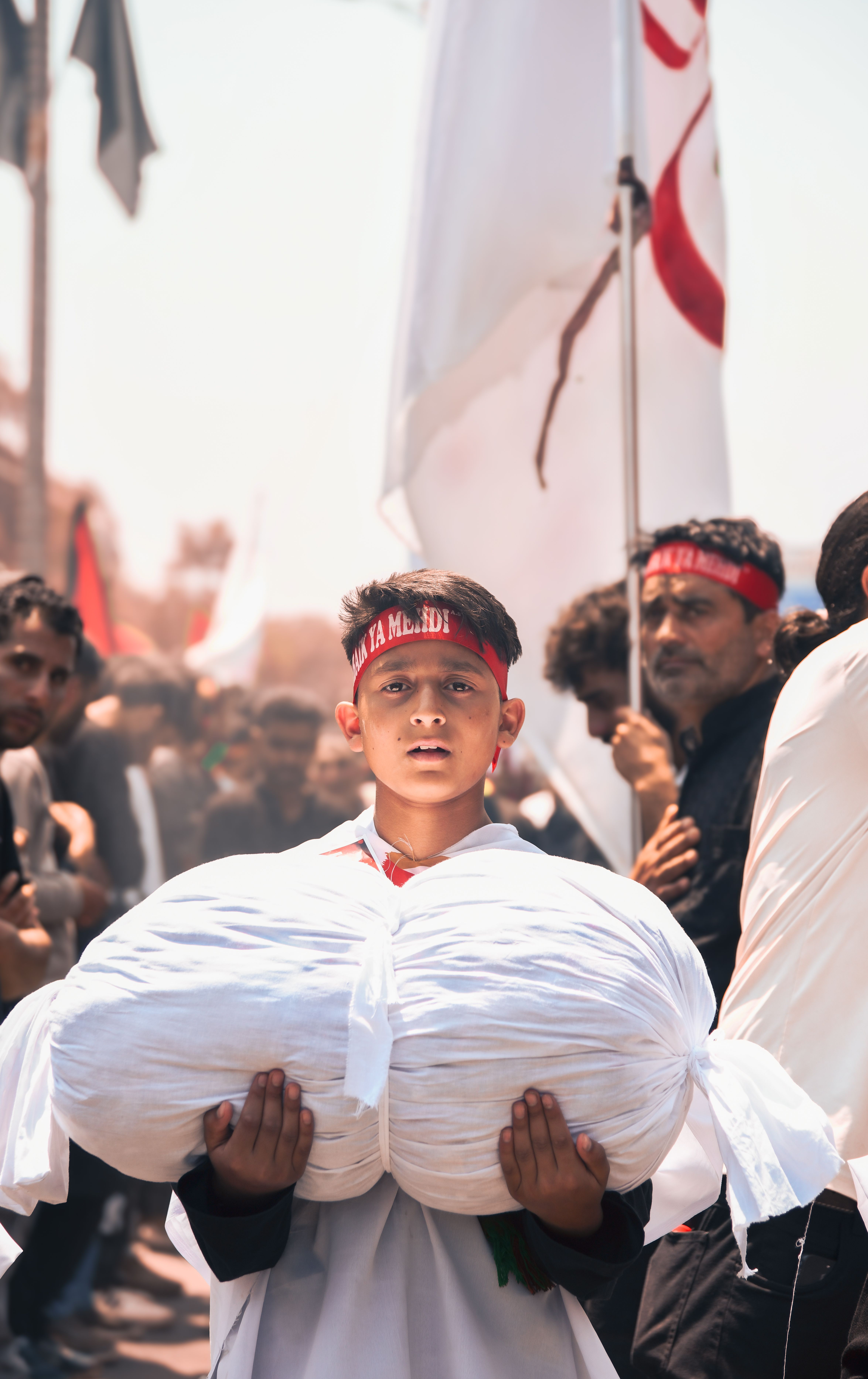 Young boy carrying white cloths in a festive street procession, surrounded by people.