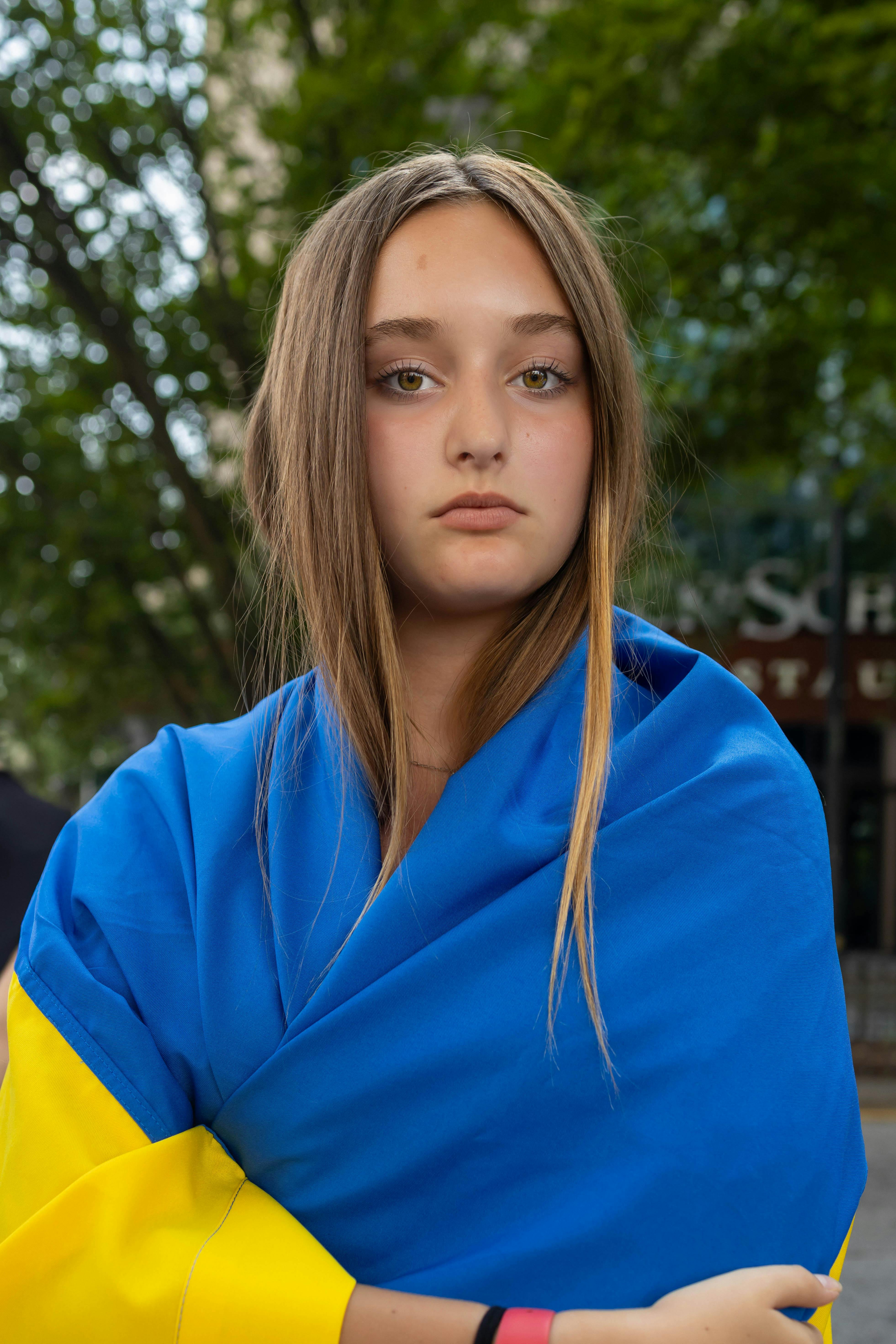 Free Portrait of a young woman outdoors wrapped in blue and yellow fabric, against a lush green backdrop. Stock Photo