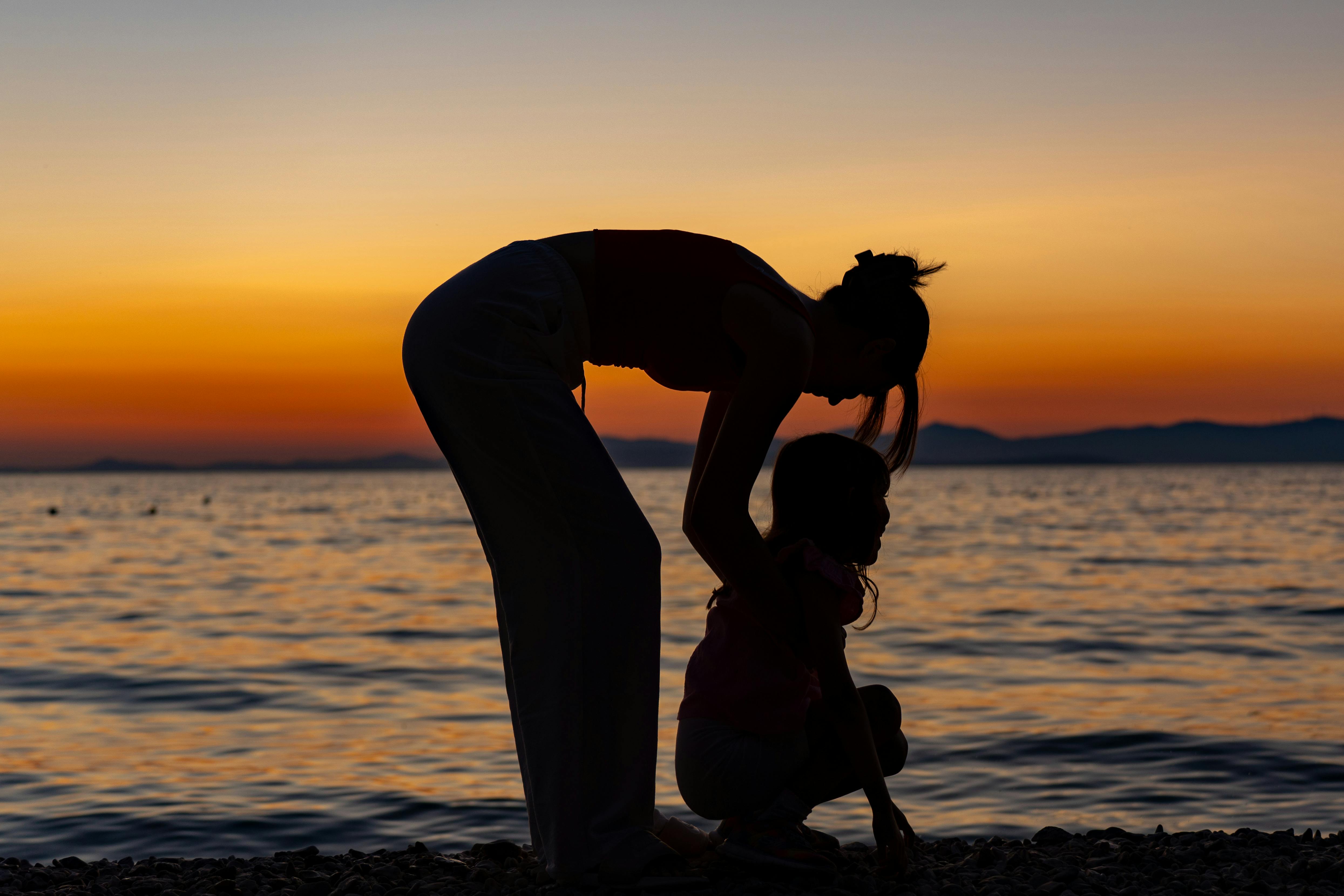 a woman and child are silhouetted against the sunset