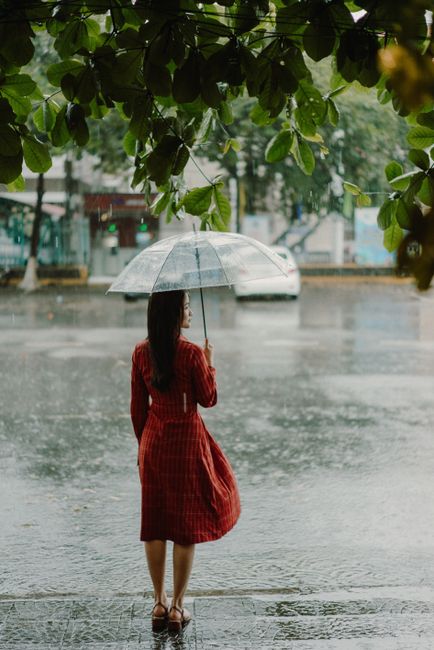 Elegant woman in a red dress holding an umbrella in rainy Hội An, Vietnam.