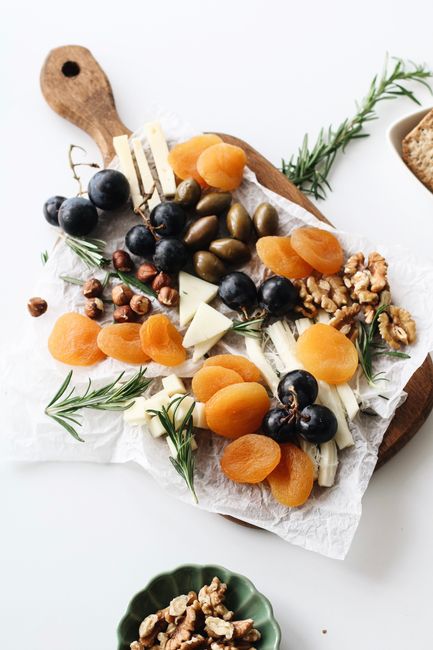 A rustic cheese platter with assorted nuts, dried fruits, and olives on a wooden board.