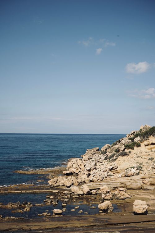 Free Serene coastal landscape with rocky cliffs and blue ocean under a clear summer sky. Stock Photo