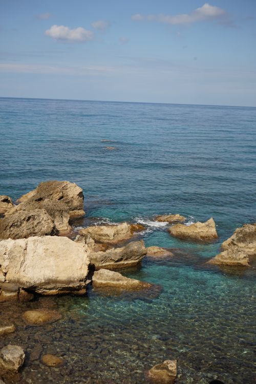 Free A stunning rocky seashore with clear blue waters under a summer sky. Stock Photo