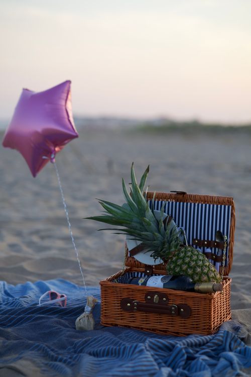 Free A serene beach scene with a picnic basket, pineapple, and star balloon at sunset. Stock Photo