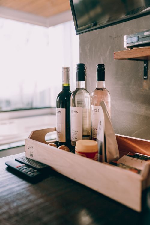 Free A collection of wine bottles with a TV remote on a wooden table, creating a cozy interior setting. Stock Photo