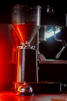 Coffee beans in a grinder illuminated by red neon light, creating a moody cafe atmosphere.