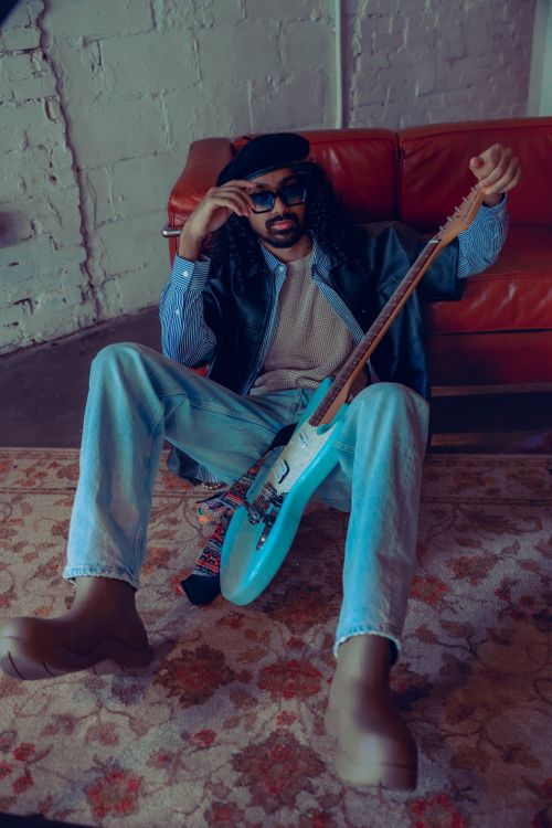 Free Trendy musician with electric guitar in chic attire sitting on a rug indoors. Stock Photo