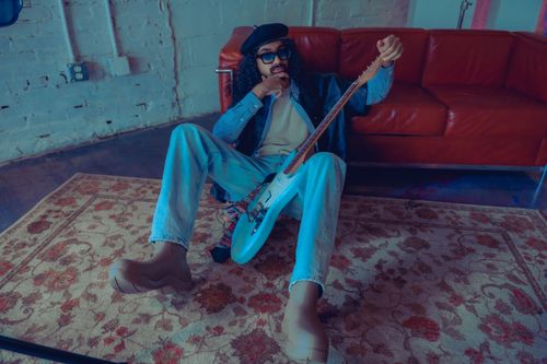 Free A fashionable musician lounges with an electric guitar in a vintage room setting, exuding artistic flair. Stock Photo