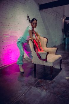 A fashionably dressed musician poses with an electric guitar in an industrial setting.