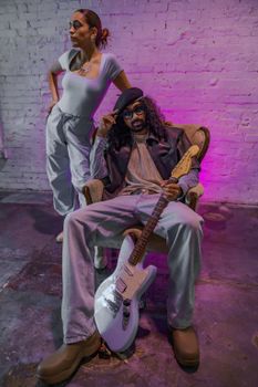Portrait of two stylish musicians with a guitar in an urban setting under vibrant lighting.