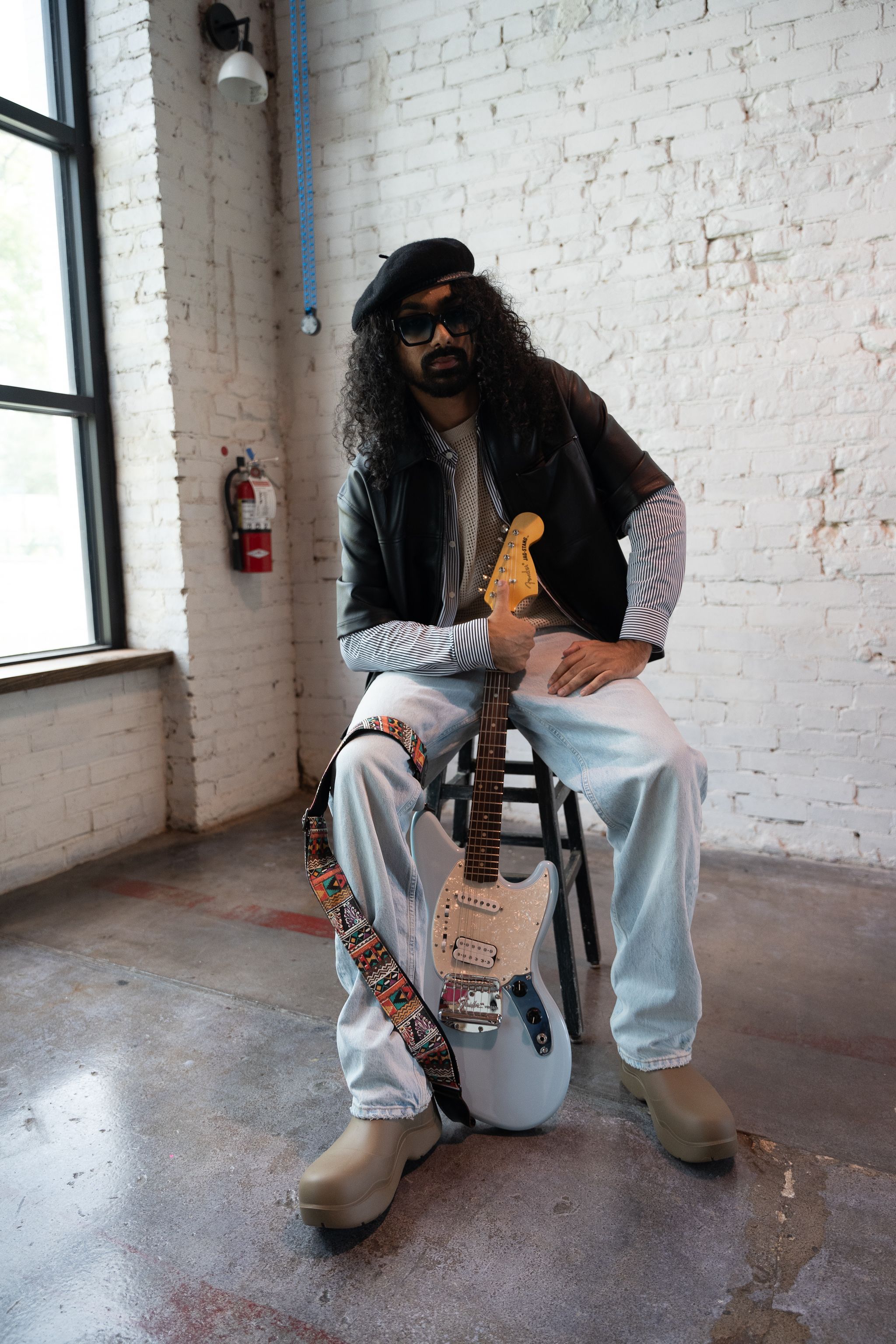 Stylish musician posing with electric guitar in an urban studio setting.