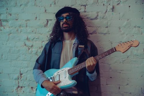 Free Portrait of a trendy musician with an electric guitar against a vintage brick wall. Stock Photo