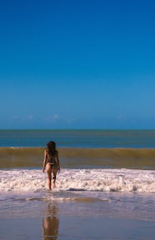 A woman walking into the ocean at Pipa Beach, Brazil on a sunny day, capturing relaxation and adventure.
